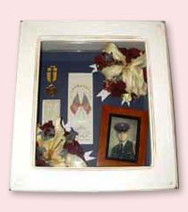 white shadow box display of preserved flowers with photo of soldier, ribbons and other military memorabilia