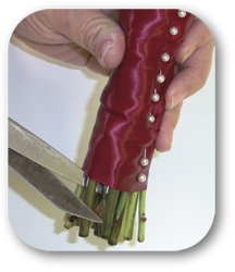 stems of bouquet wrapped in ribbon being cut diagonally with scissors