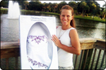 smiling woman in front of lake holding wedding gown preservation chest with preserved gown